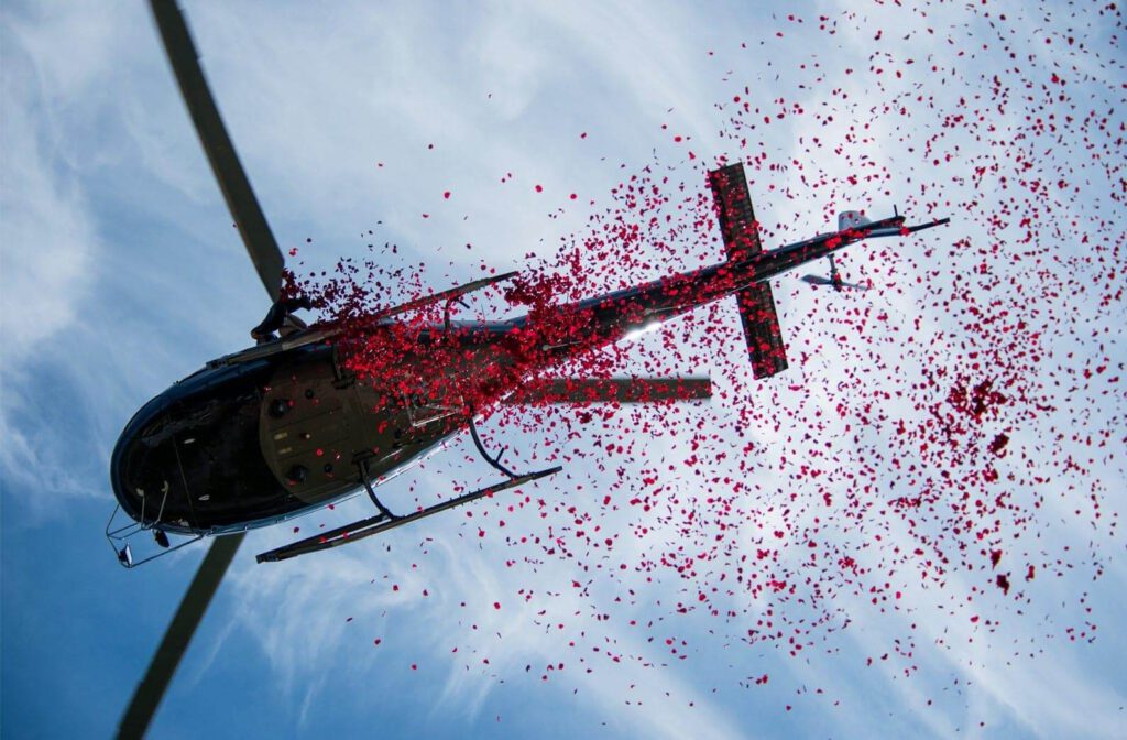Helikopter verteilt rote Rosenblätter aus der Luft über eine Feier.